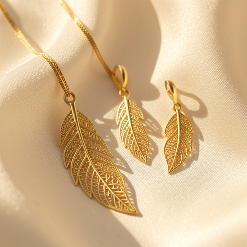 Ensemble de bijoux dorés en forme de plume, délicatement disposés sur un tissu de soie ivoire dans une ambiance élégante et lumineuse.