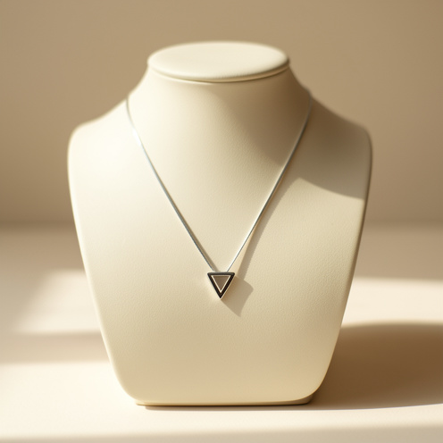 Collier fin à pendentif triangulaire, présenté avec élégance sur un support ivoire dans une ambiance lumineuse et minimaliste.