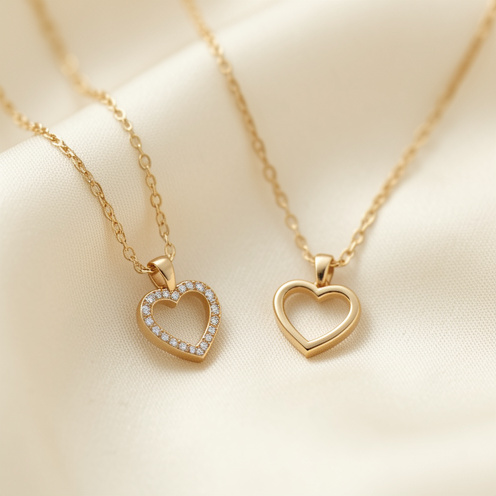Deux colliers délicats en or avec pendentifs en forme de cœur, disposés sur une soie ivoire.