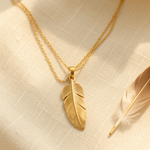 Collier délicat en or avec pendentif en forme de plume, présenté sur un tissu en lin crème dans une lumière douce et chaleureuse.