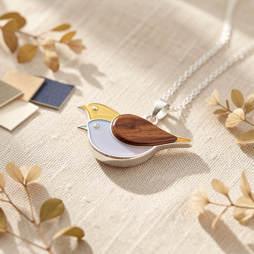 Pendentif en forme d’oiseau présenté avec plusieurs matières et éléments botaniques sur un tissu en lin naturel.