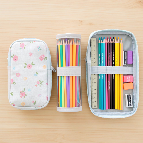 Trois trousses à crayons de formats différents, garnies de fournitures scolaires et disposées sur un bureau en bois clair.